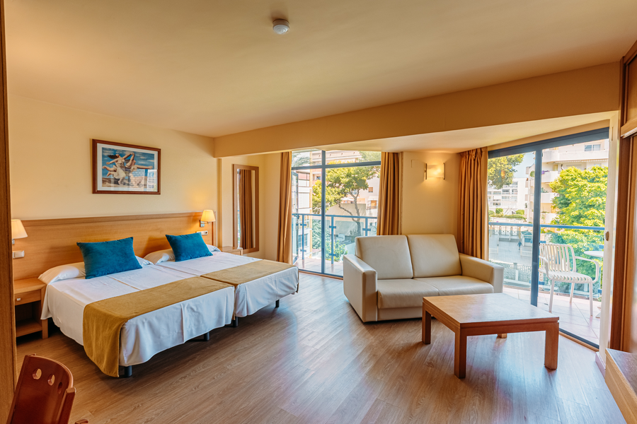 Habitación de hotel con dos camas, sofá y balcón. MS hoteles: Puerto Marina vista.