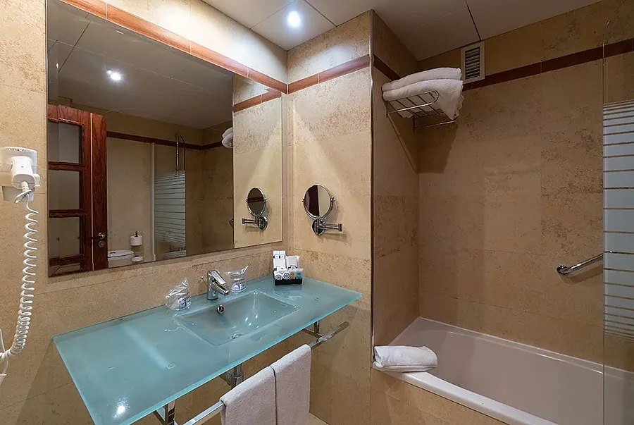Baño moderno con lavabo de cristal, ducha y toallas limpias. MS: Maestranza