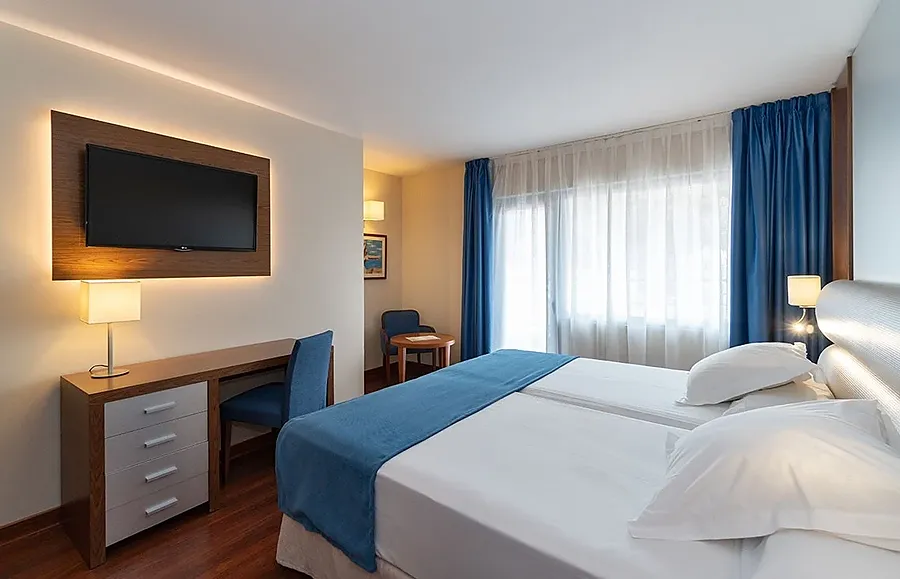 Habitación de hotel con dos camas, escritorio y TV. MS: Maestranza