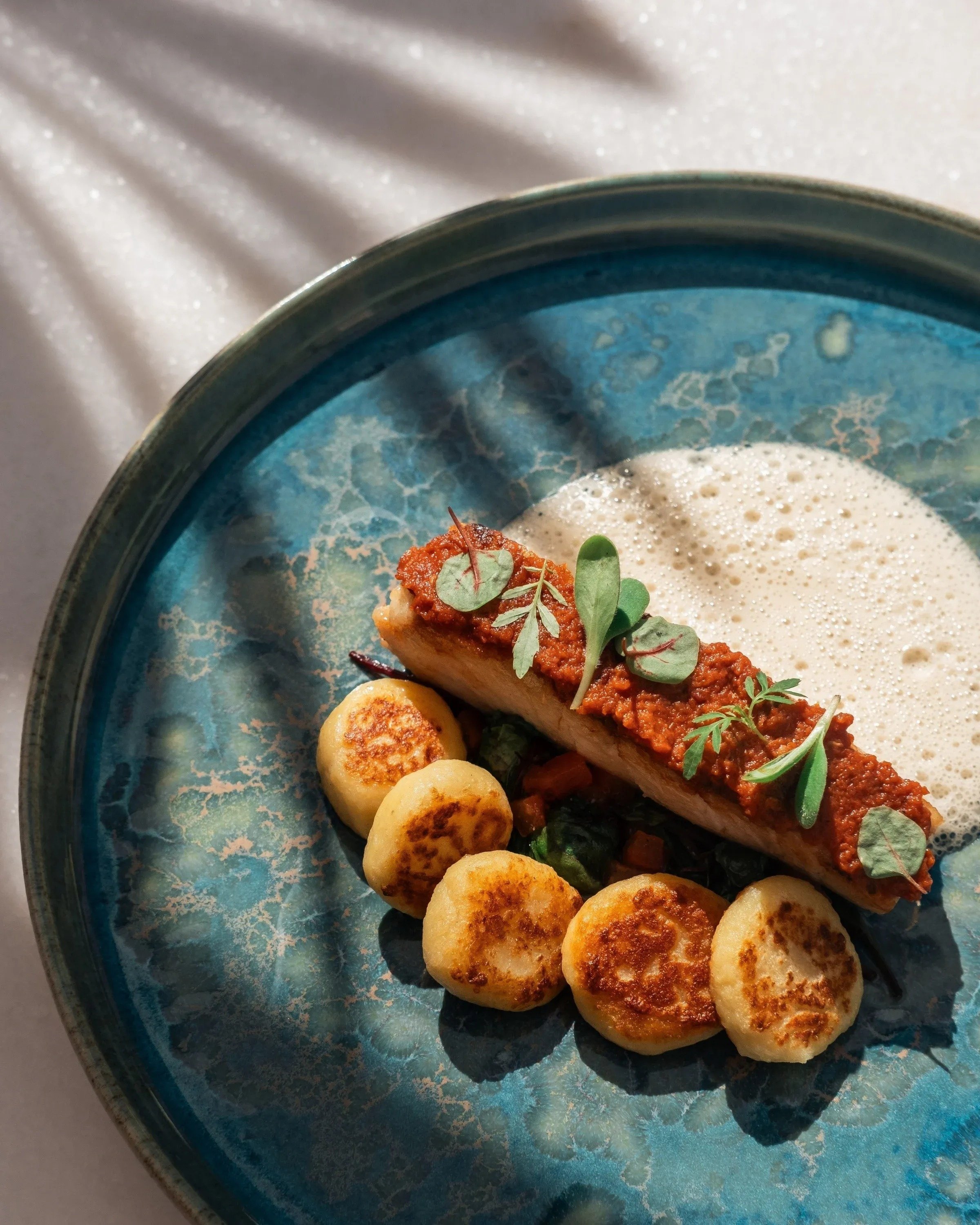 a blue plate topped with a piece of meat and gnocchi