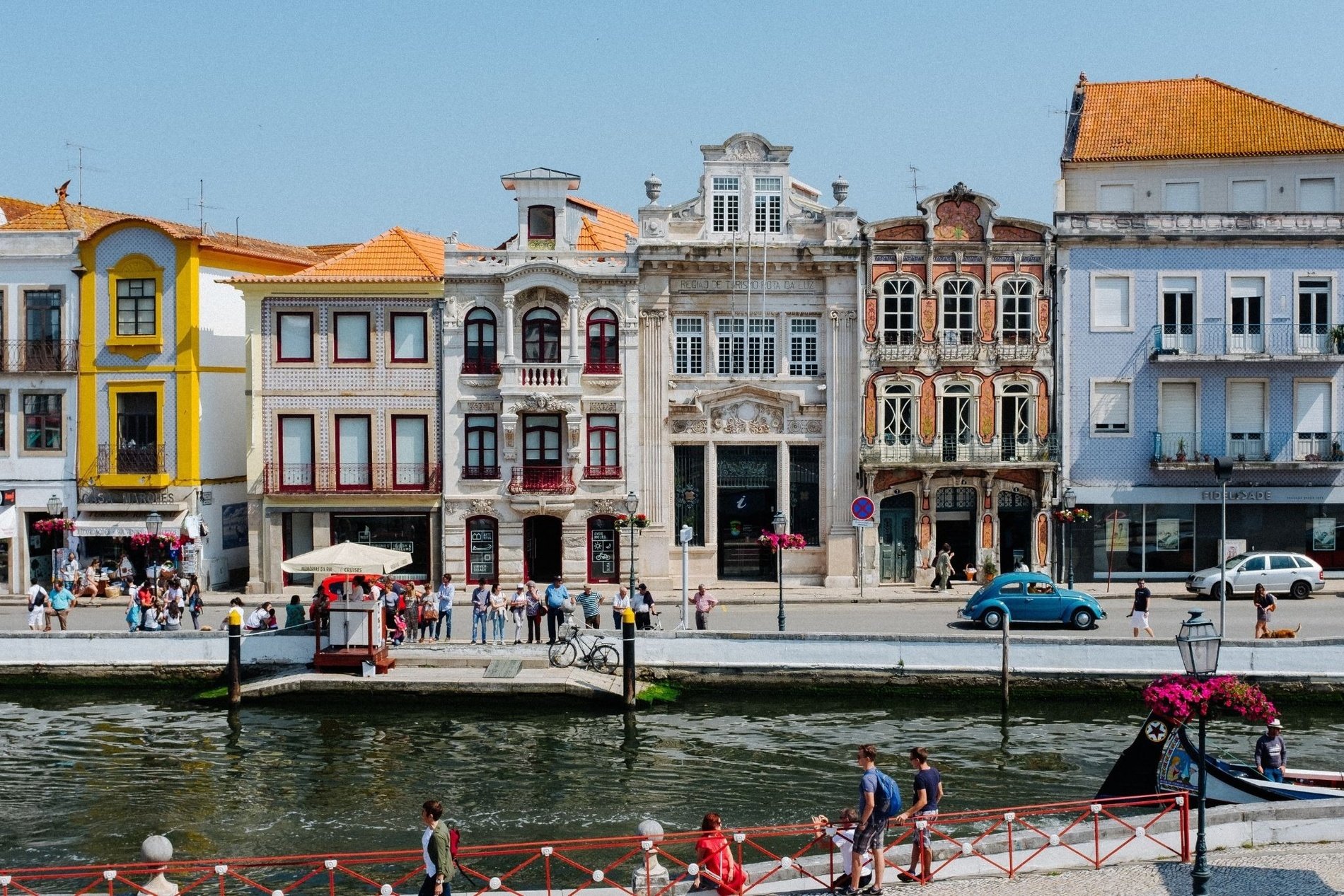um grupo de pessoas caminha ao longo de uma ponte sobre um rio cercado por edifícios coloridos