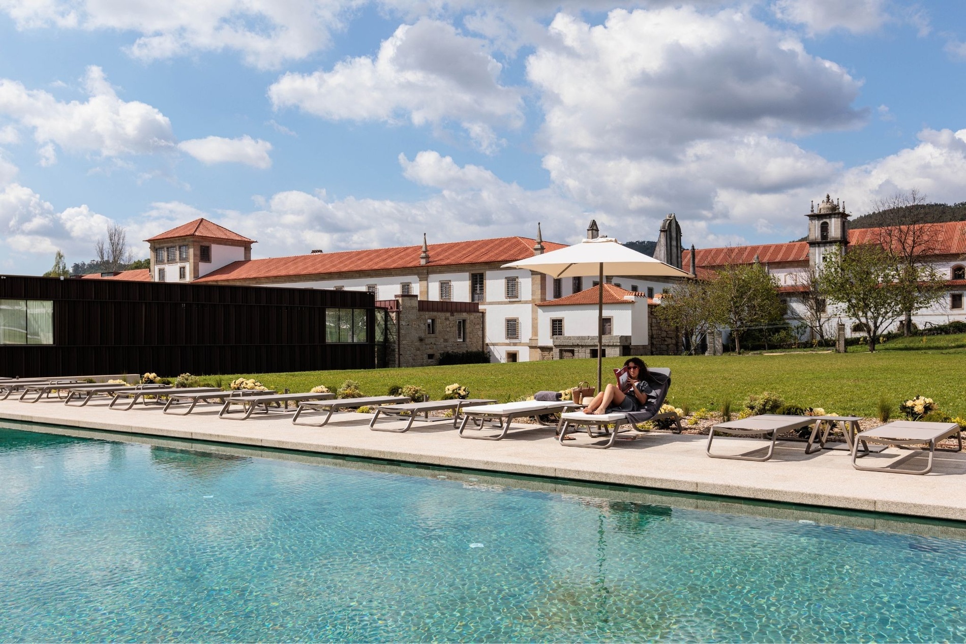 a woman sits on a lounge chair near a swimming pool