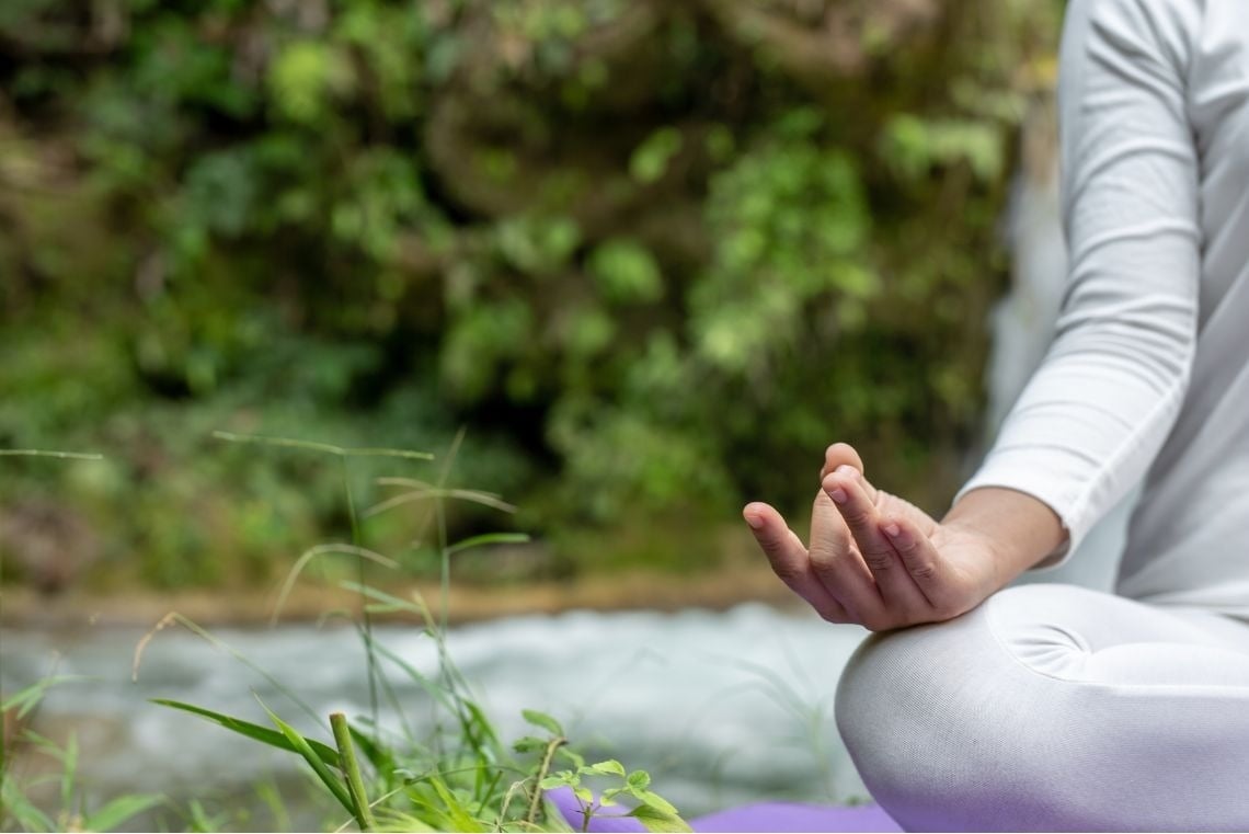 una mujer está sentada en una alfombra de yoga junto a un río