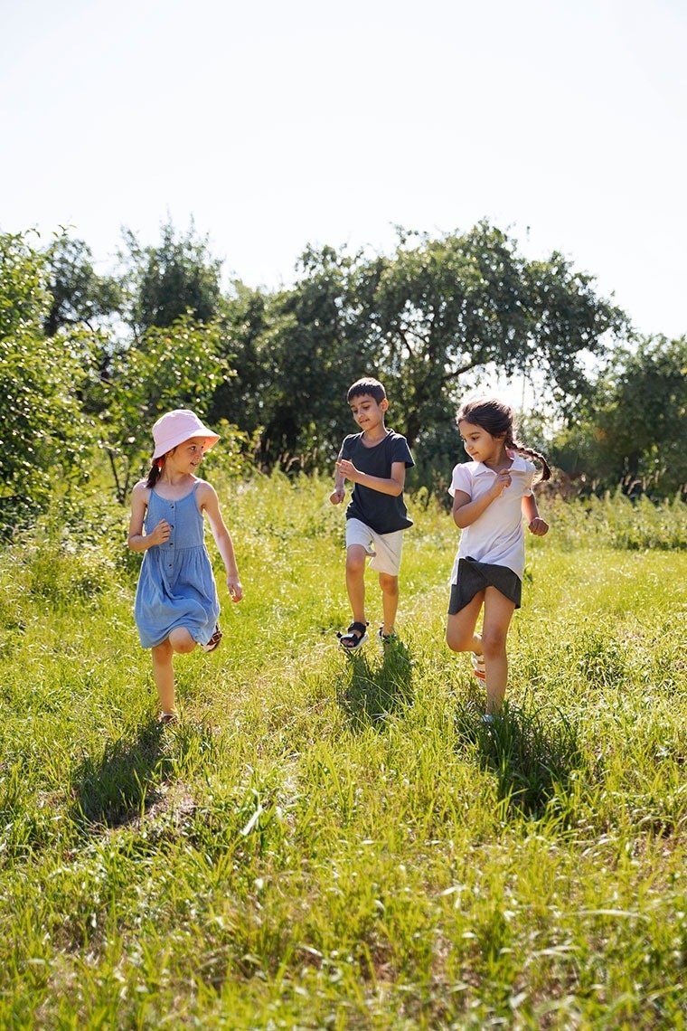 un niño y dos niñas corriendo por un campo de hierba