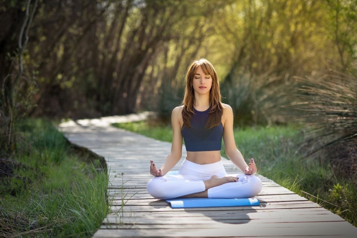 una mujer está sentada en una pose de yoga en un muelle de madera