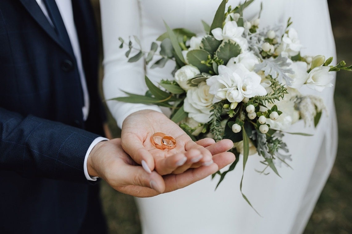 una novia y un novio sostienen anillos de boda en sus manos