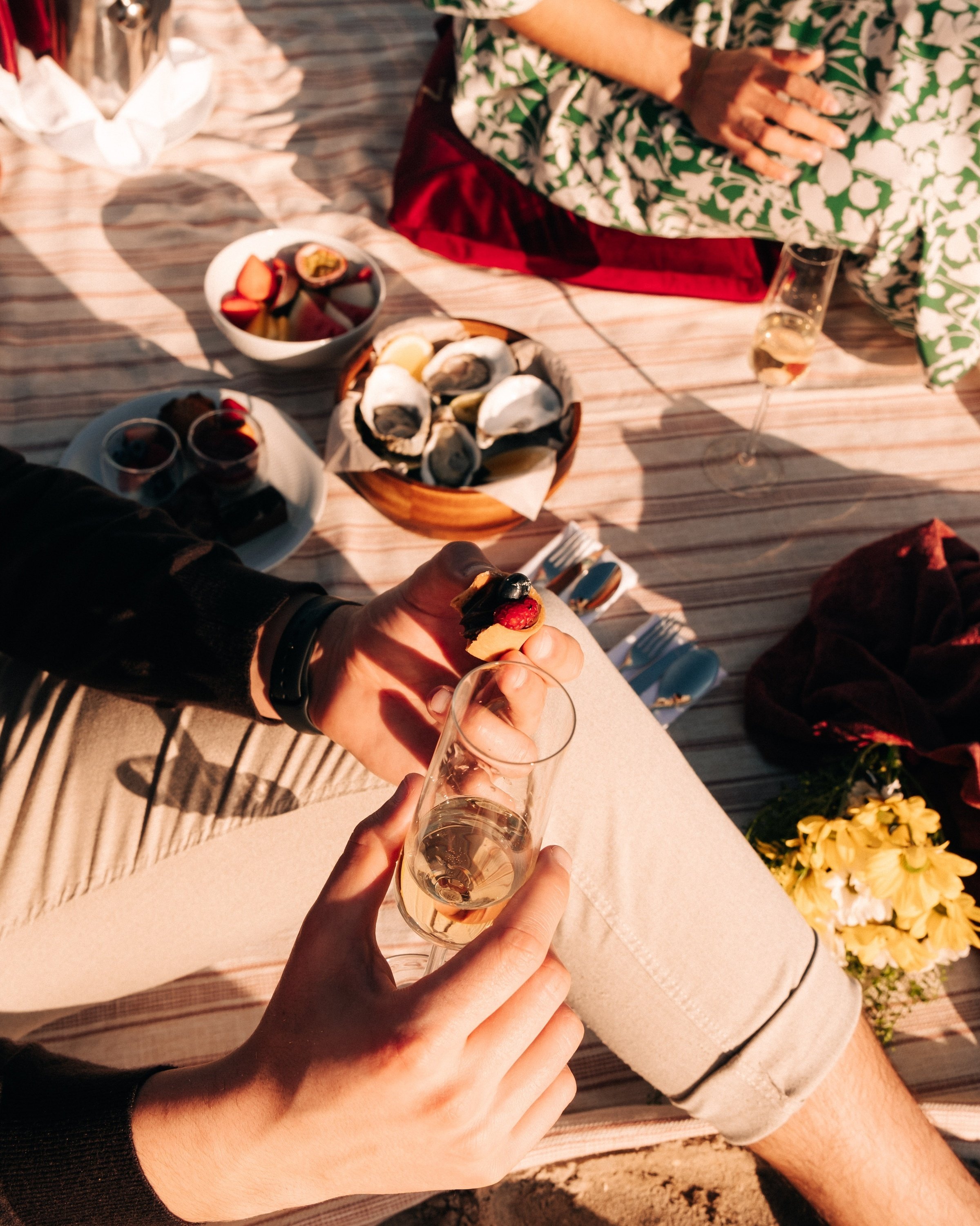 dos mujeres están comiendo ostras en un picnic en la playa