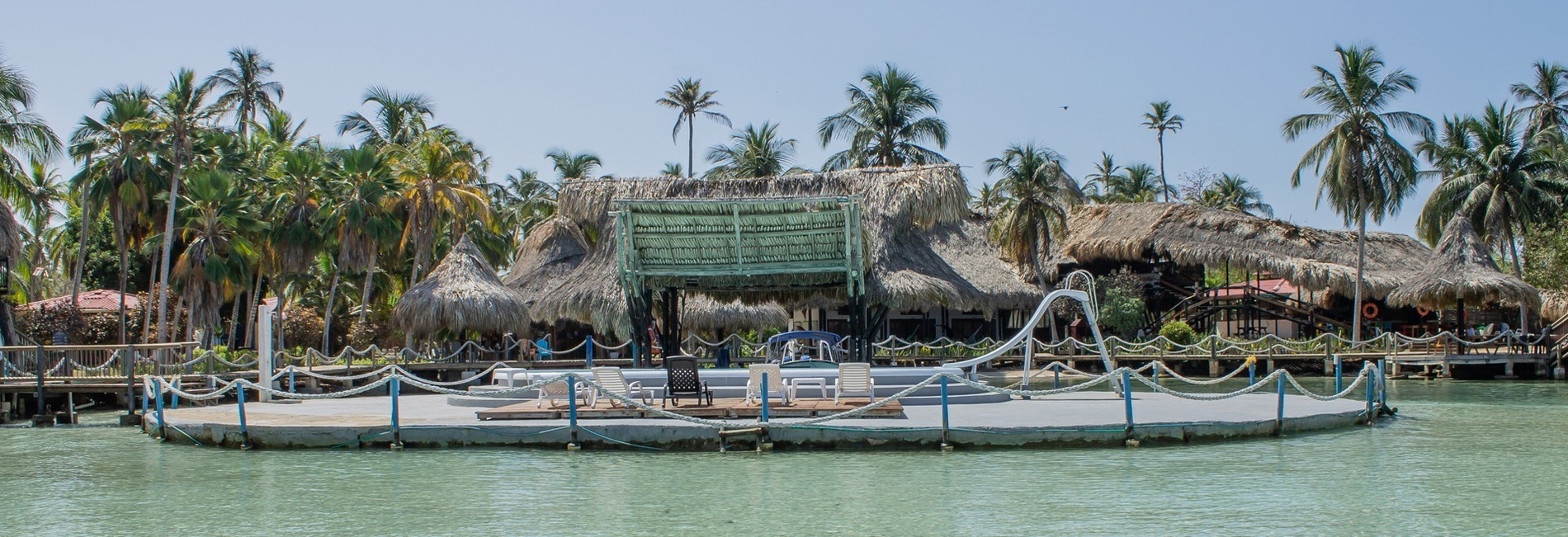 a dock in the middle of a body of water surrounded by palm trees