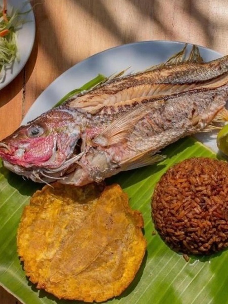 un plato de pescado frito con arroz y tostones en una hoja de plátano