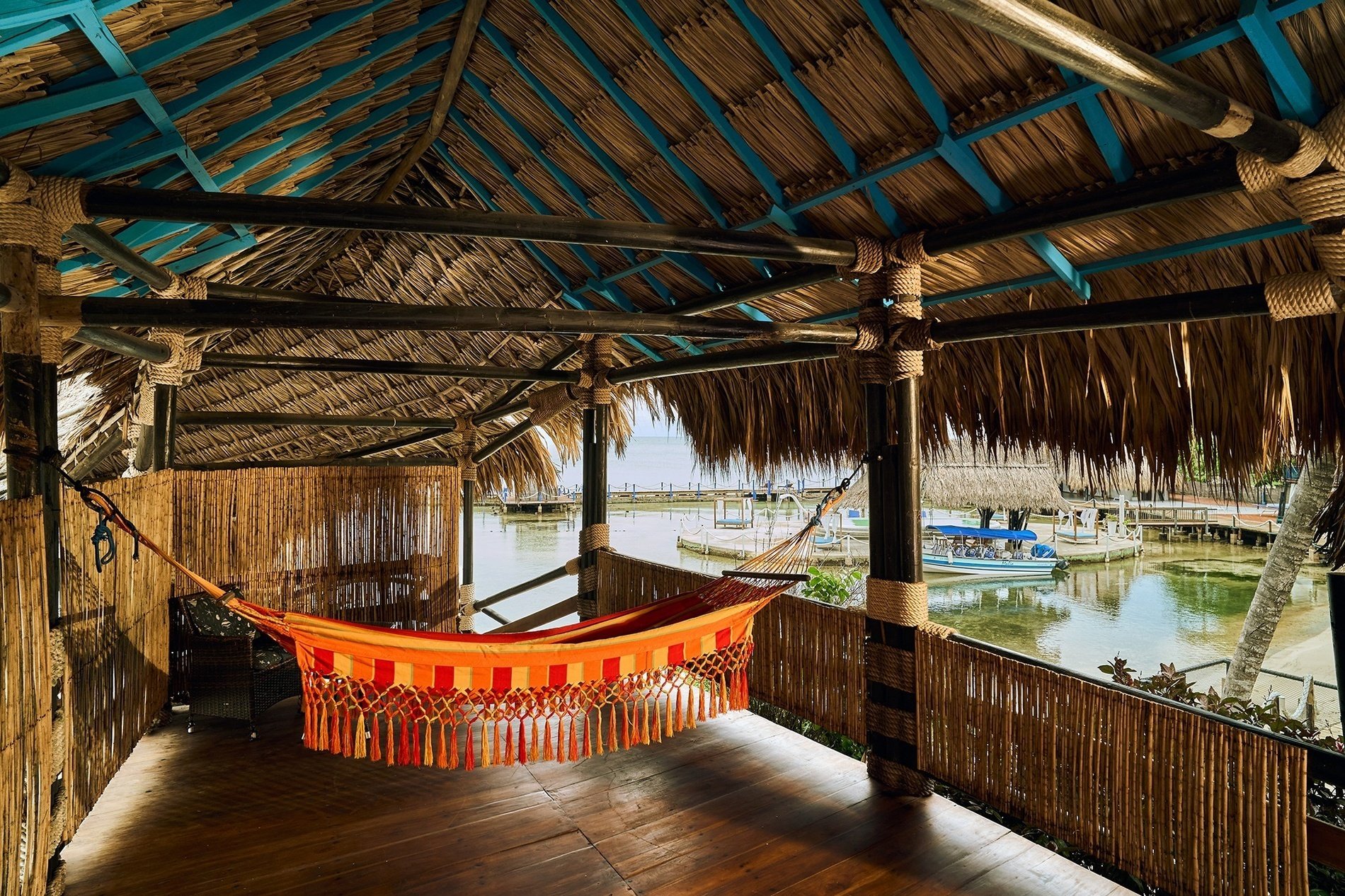 a hammock hangs from a thatched roof overlooking a body of water