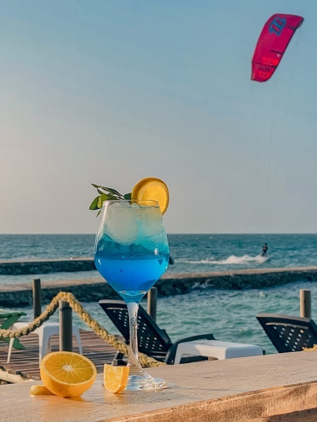 un cóctel azul con una rodaja de limón sobre una mesa de madera con un parapente volando en el fondo