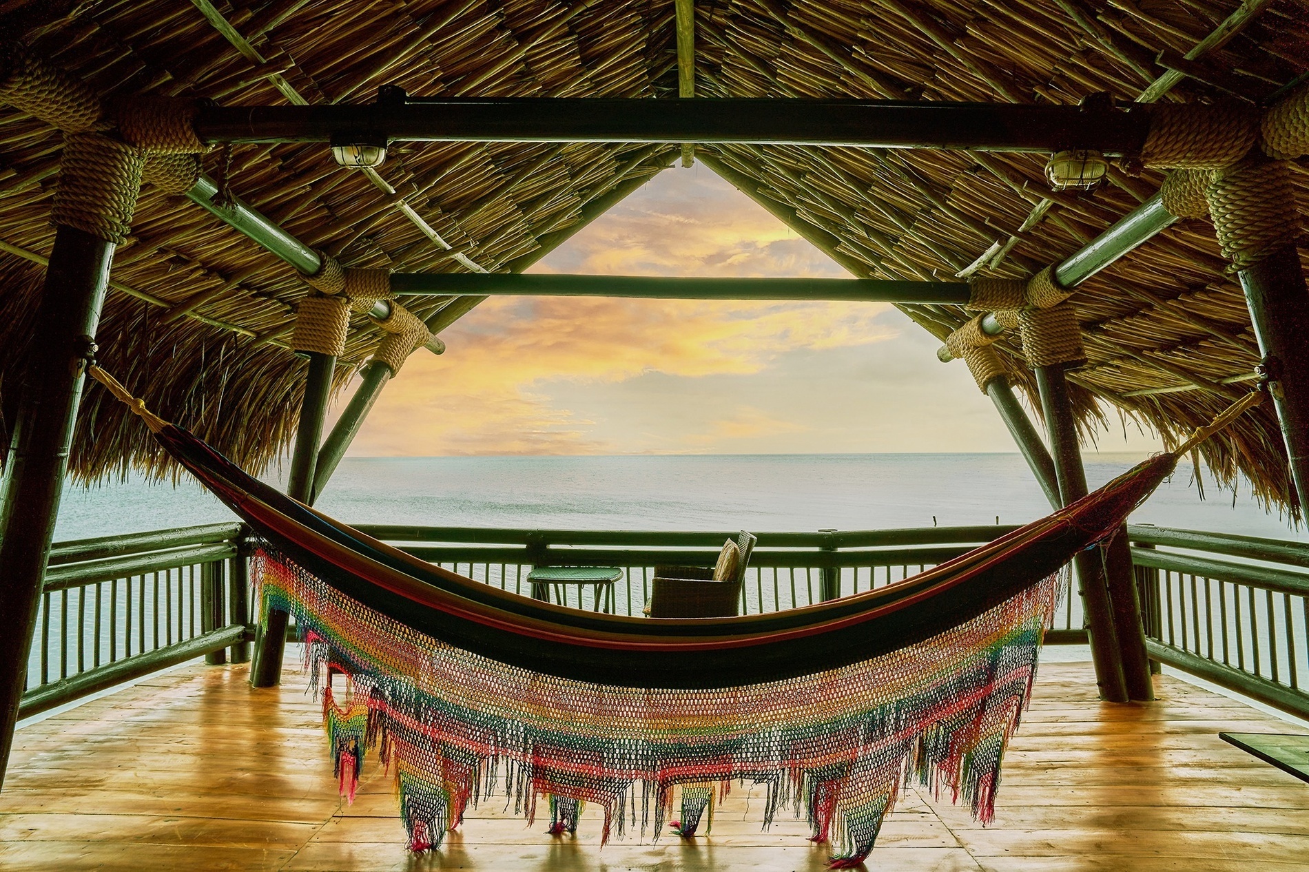 a colorful hammock hangs from a thatched roof overlooking the ocean