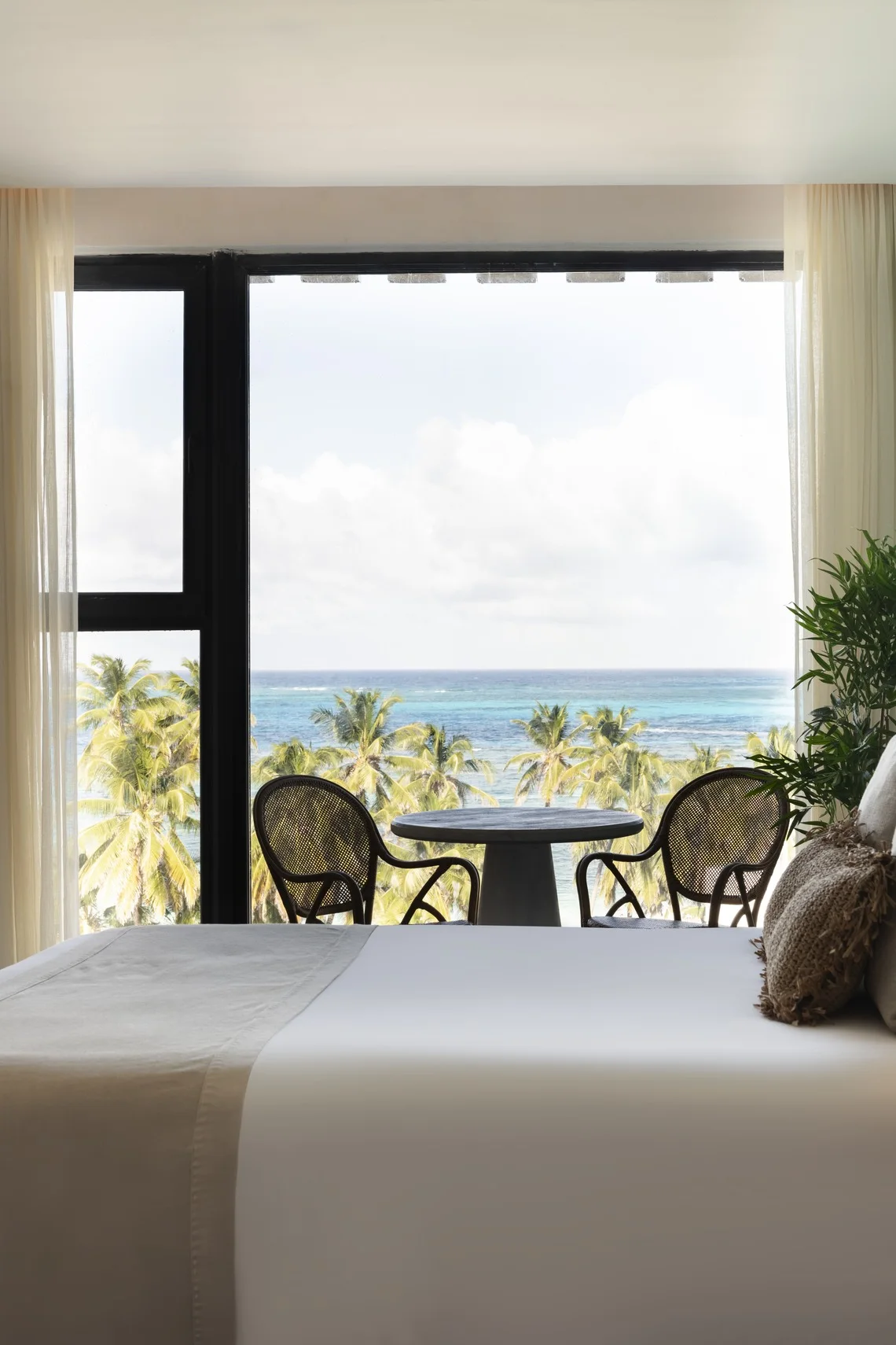 Quarto de hotel com vista para o mar, palmeiras e uma mesa com cadeiras. Nattivo Collection Hotel