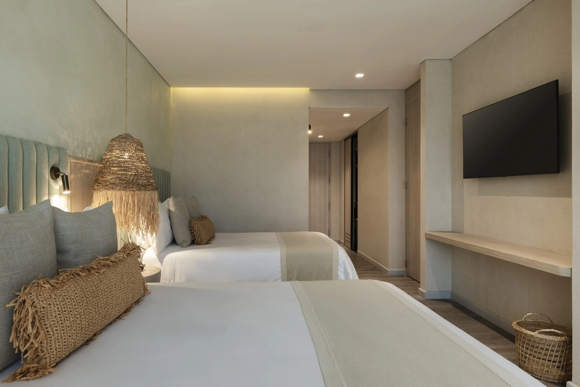 Quarto de hotel com duas camas,Nattivo Collection Hotel, luminária de vime e TV.