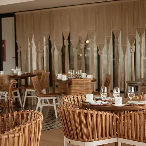 Comedor estilo bohemio en hotel. Nattivo Collection Hotel con mesas de ratán y sillas para cenas.