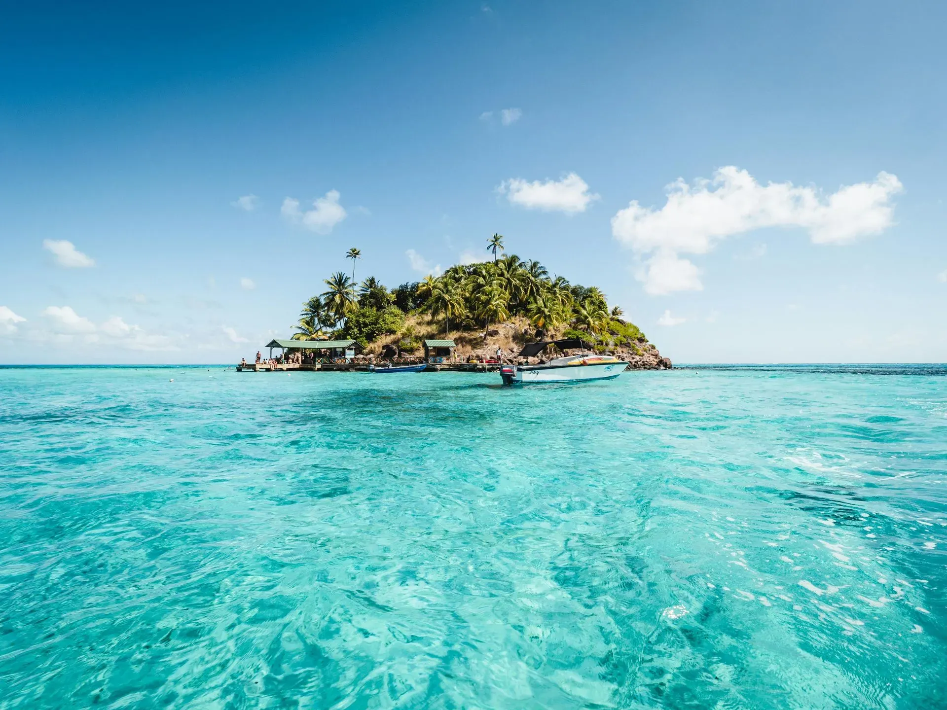 Tropical island resort with turquoise waters and a boat, ideal for a Nattivo Collection Hotel getaway.