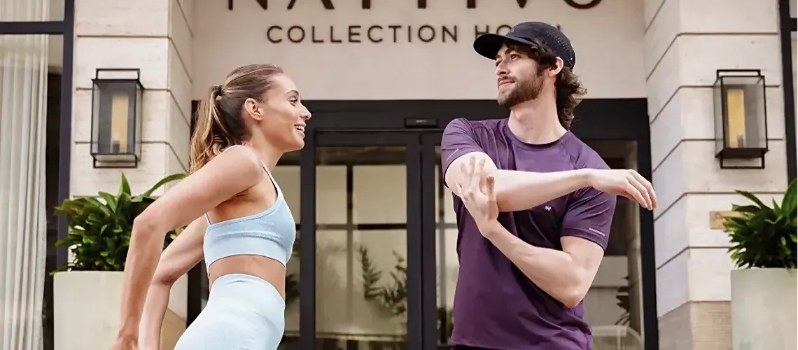 Casal sorrindo ao se alongar em frente ao Nattivo Collection Hotel nativo.