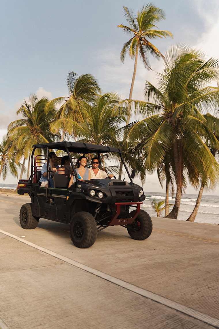 People enjoy an off-road Nattivo Collection Hotel adventure near a tropical beach with palm trees.