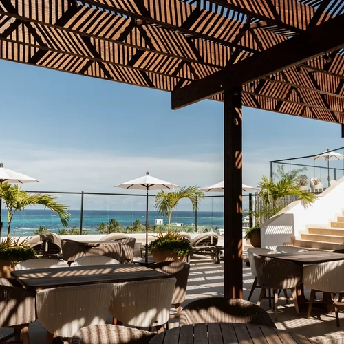 Terraza de hotel con vista al mar, mesas y sillas estilo mimbre, palmeras y sombrillas. Nattivo Collection Hotel