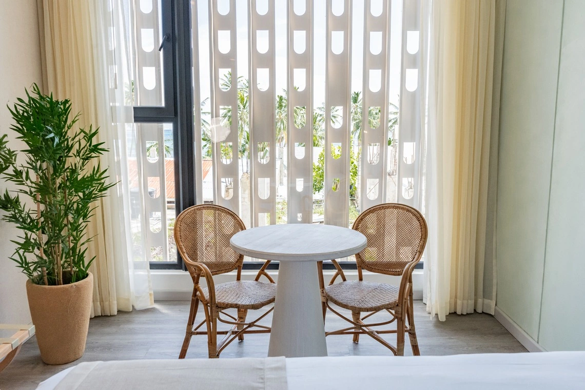 Mesa com cadeiras de vime em quarto de hotel com vista para o mar, perto da janela comNattivo Collection Hotel.