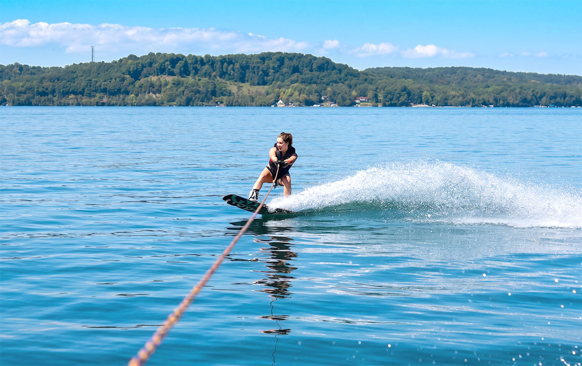 Mulher wakeboardando em lago calmo, com montanhas verdejantes ao fundo. Nattivo Collection Hotel para aventura.