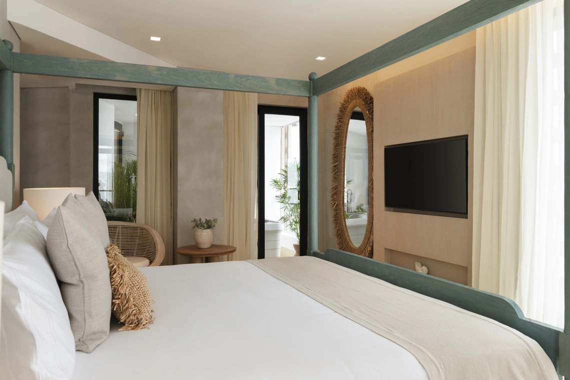 Cama de Nattivo Collection Hotel moderna com espelho oval e TV, em quarto de hotel com vista para varanda.
