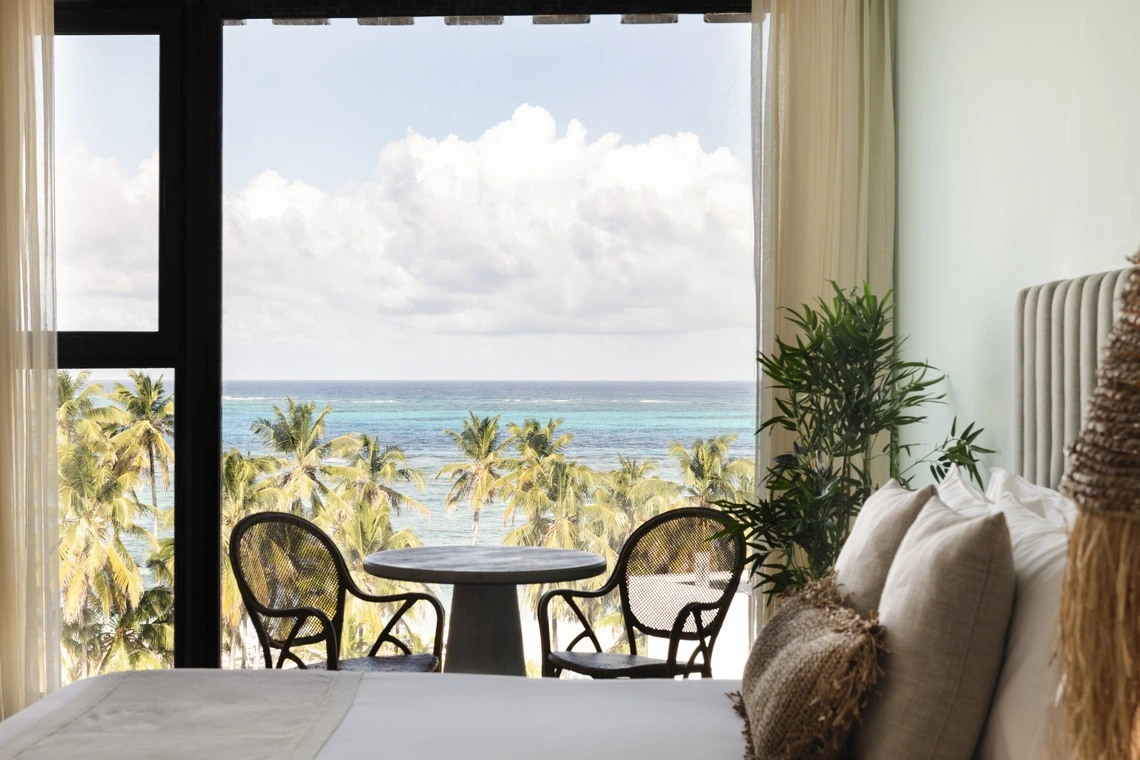 Vista do quarto para o mar e coqueiros com mesa e cadeiras Nattivo Collection Hotel.