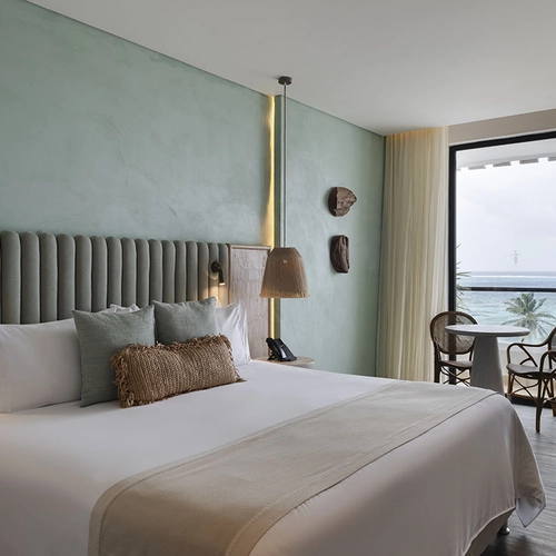 Dormitorio con vista al mar y balcón, Nattivo Collection Hotel con cama King y mesa con sillas.