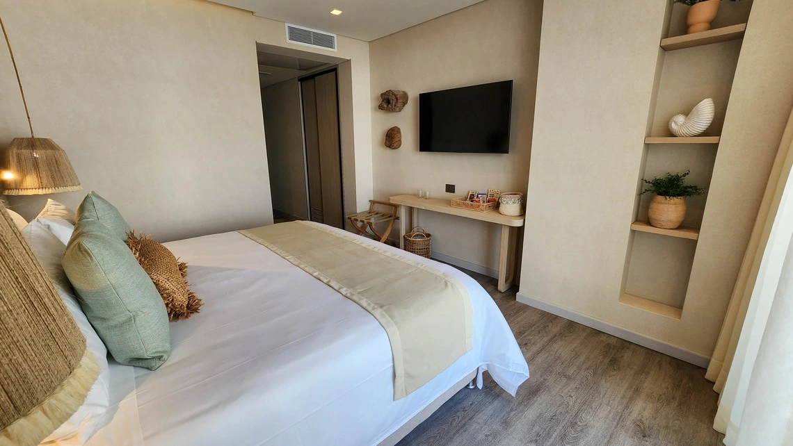 Quarto de hotel com cama confortável, decoração em tons terrosos e TV. Nattivo Collection Hotel