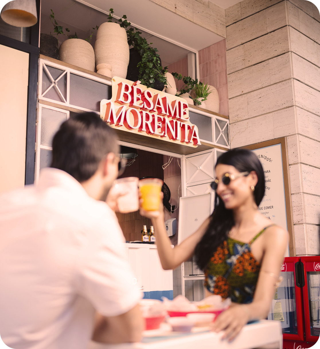 Casal brinda com drinques em frente a uma barra com a placa "Besame Morenita" Nattivo Collection Hotel.