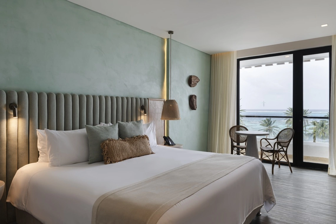 Quarto de hotel elegante com vista para o mar, uma cama confortável e uma mesa com cadeiras. Nattivo Collection Hotel