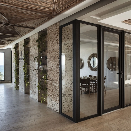 Pasillo moderno con vista al mar Nattivo Collection Hotel, plantas colgantes y puertas de vidrio hacia un comedor.