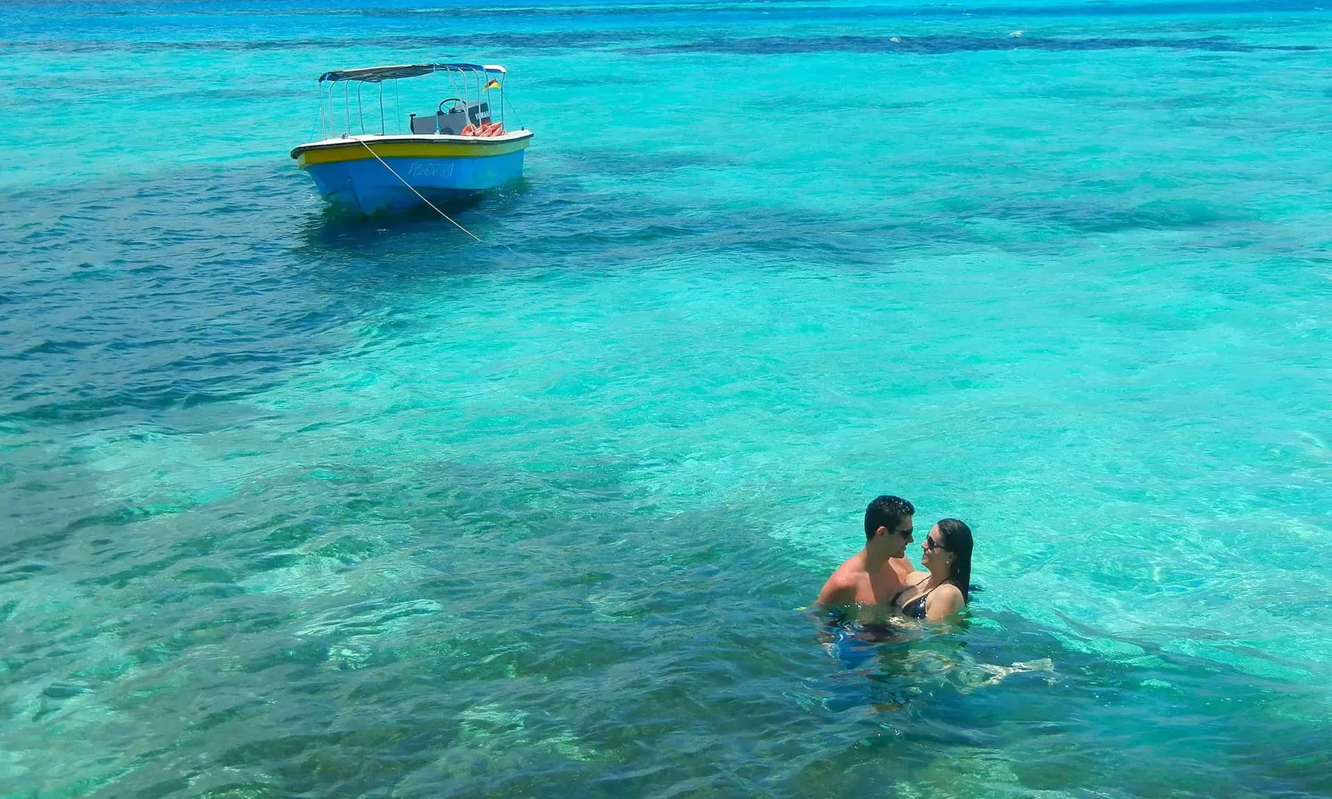 Couple swimming in clear turquoise water near a boat Nattivo Collection Hotel vacation.