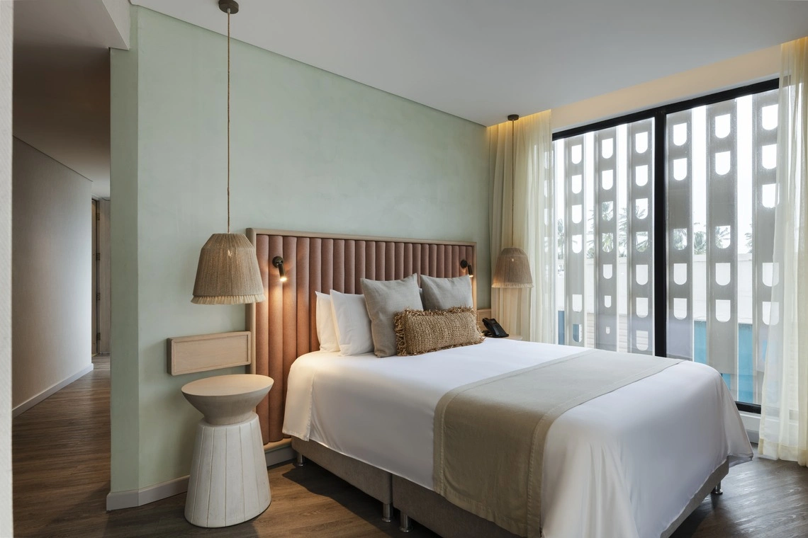 Quarto de hotel com cama king-size, cabeceira estofada e decoração tropical. Nattivo Collection Hotel