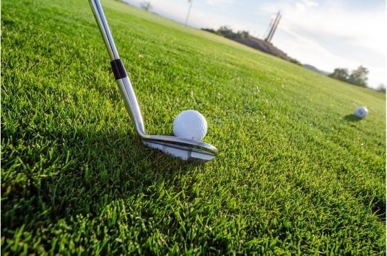 un gros plan d' un club de golf frappant une balle de golf sur un terrain de golf .