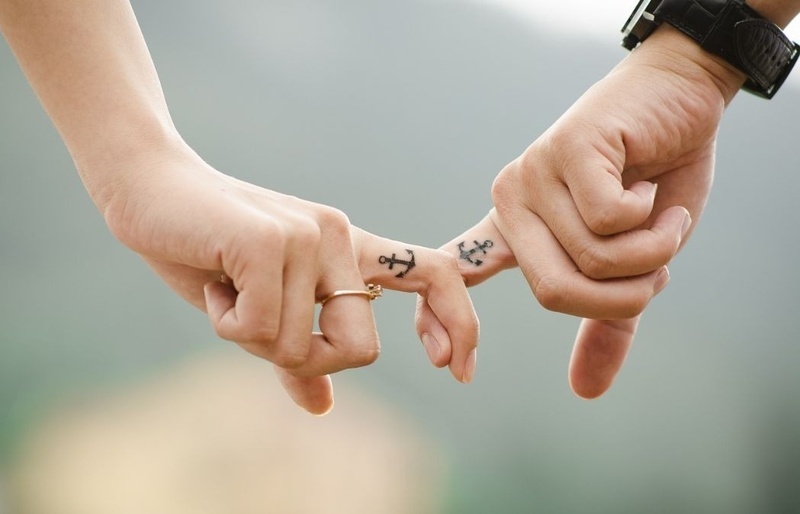 a man and woman holding hands with anchor tattoos on their fingers