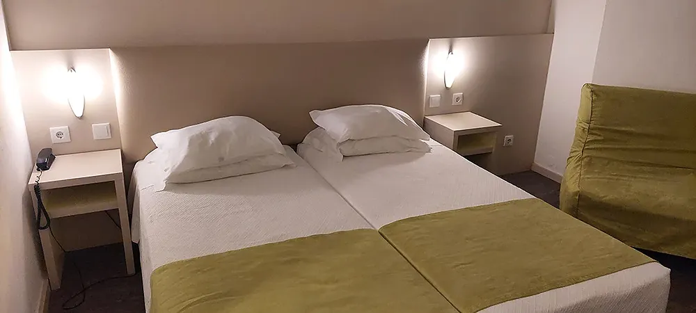 Cama de hotel com colcha verde, mesas de cabeceira e sofá verde. Navegadores para uma estadia confortável.