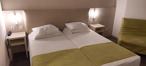 Navegadores: Quarto de hotel moderno com duas camas, mesas de cabeceira e sofá verde.