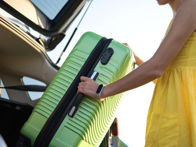 une femme porte une valise verte dans le coffre d' une voiture