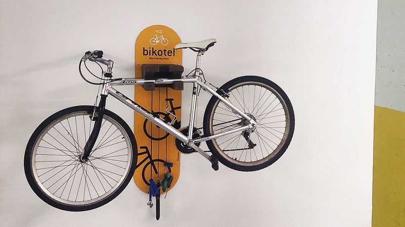 A silver bicycle is neatly hung on a yellow wall-mounted rack that says 