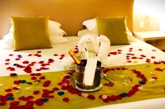 een hotelkamer met een bed versierd met rozenblaadjes en een fles champagne .
