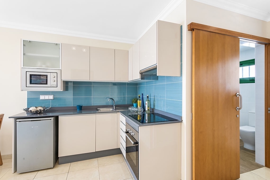 eine kleine Küche mit blauen Fliesen und weißen Schränken