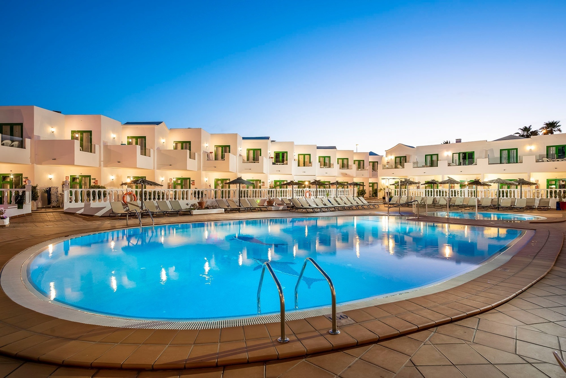 une piscine avec des chaises et des parasols au coucher du soleil