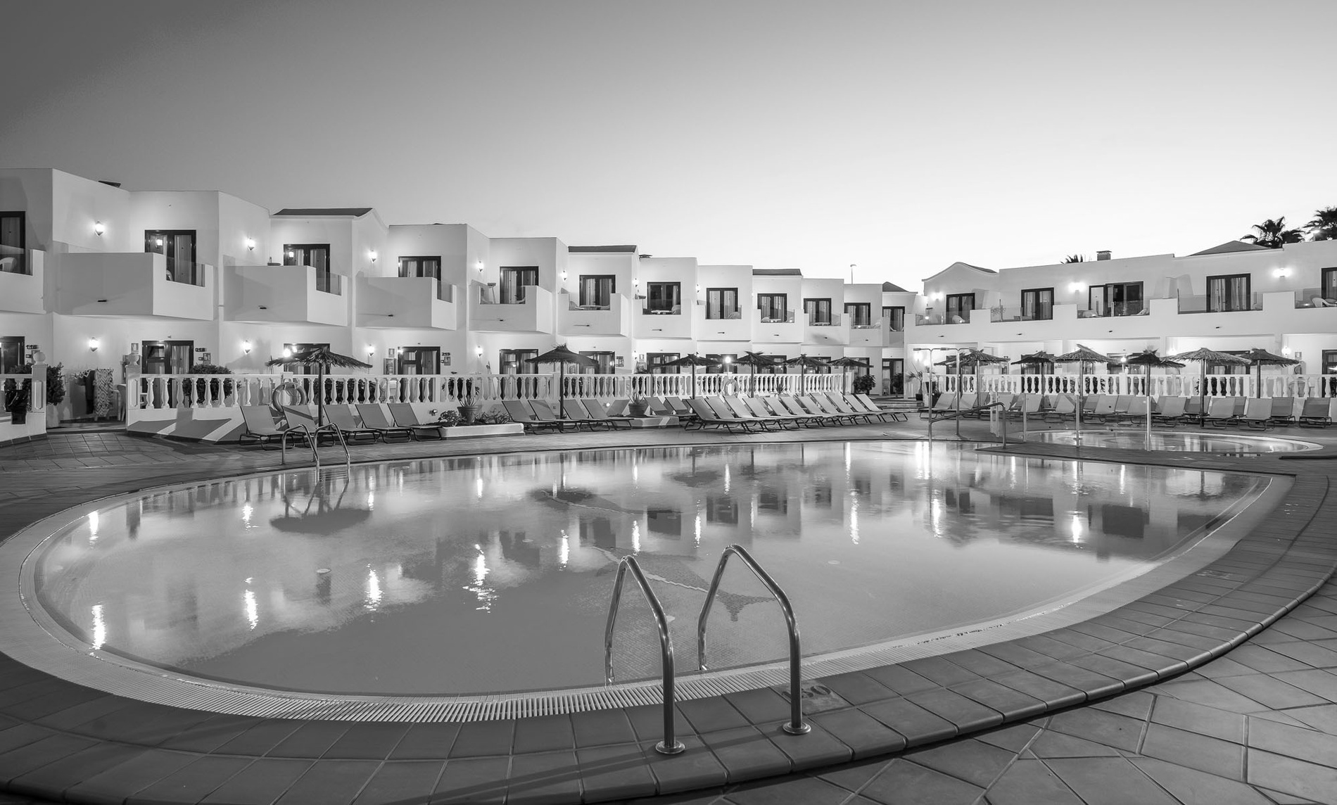 una piscina circondata da sedie e ombrelloni è illuminata al tramonto=s1900