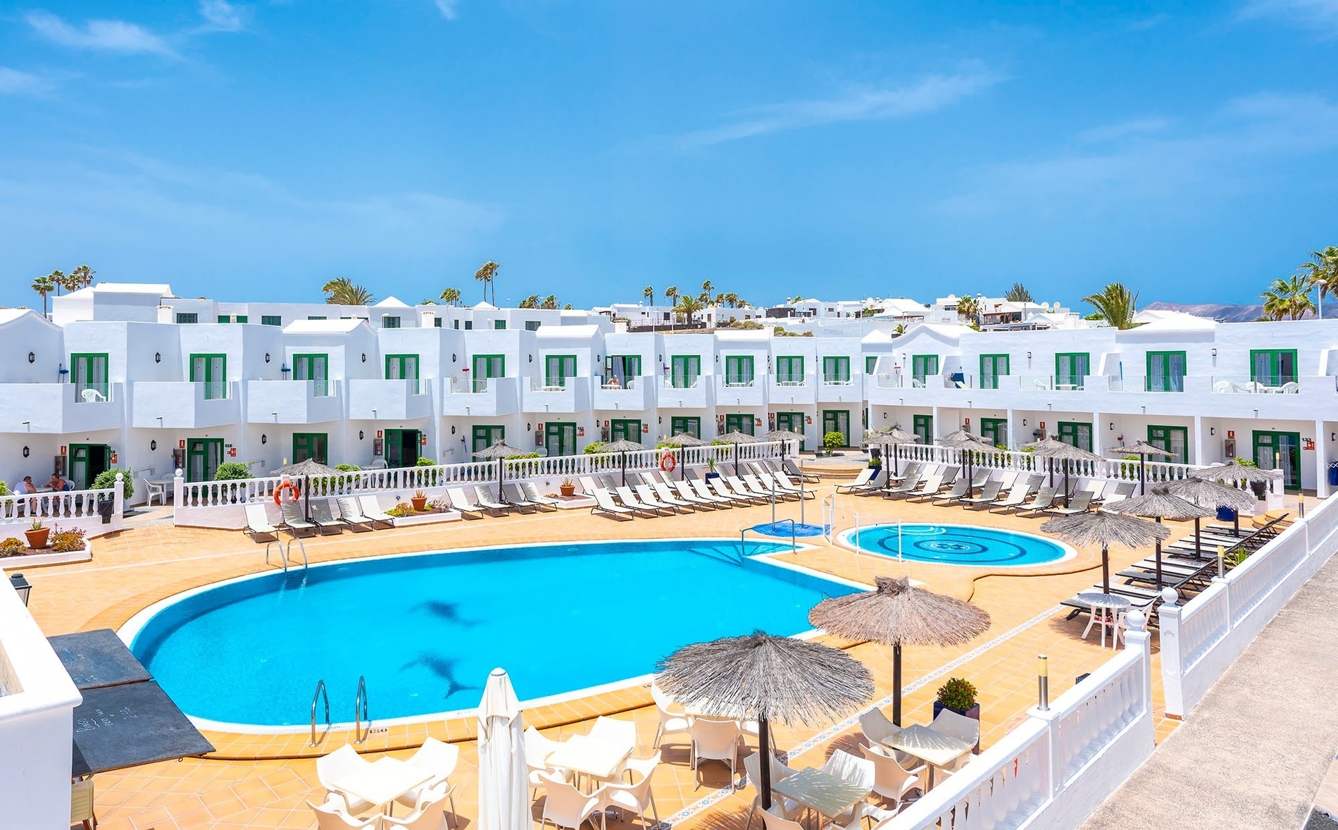 two lounge chairs under an umbrella with a hammock in the background