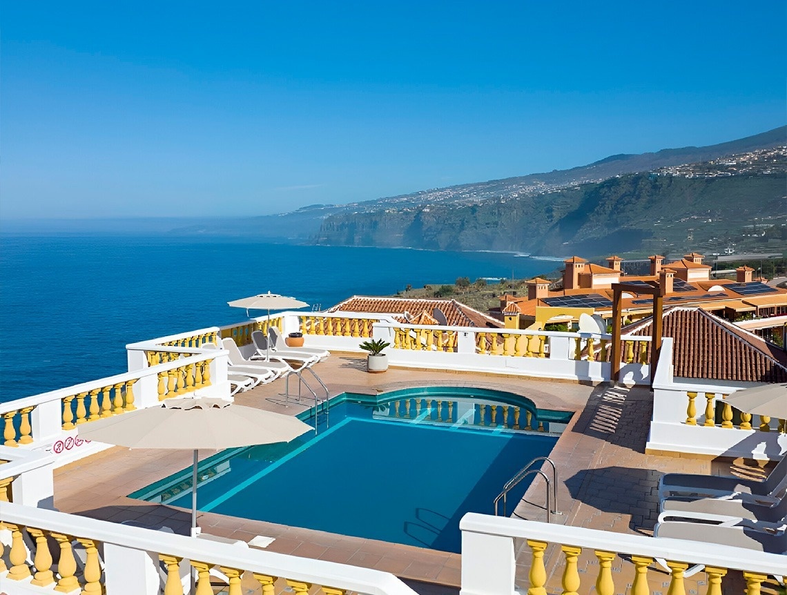 una hamaca y un paraguas en un balcón con vista al océano