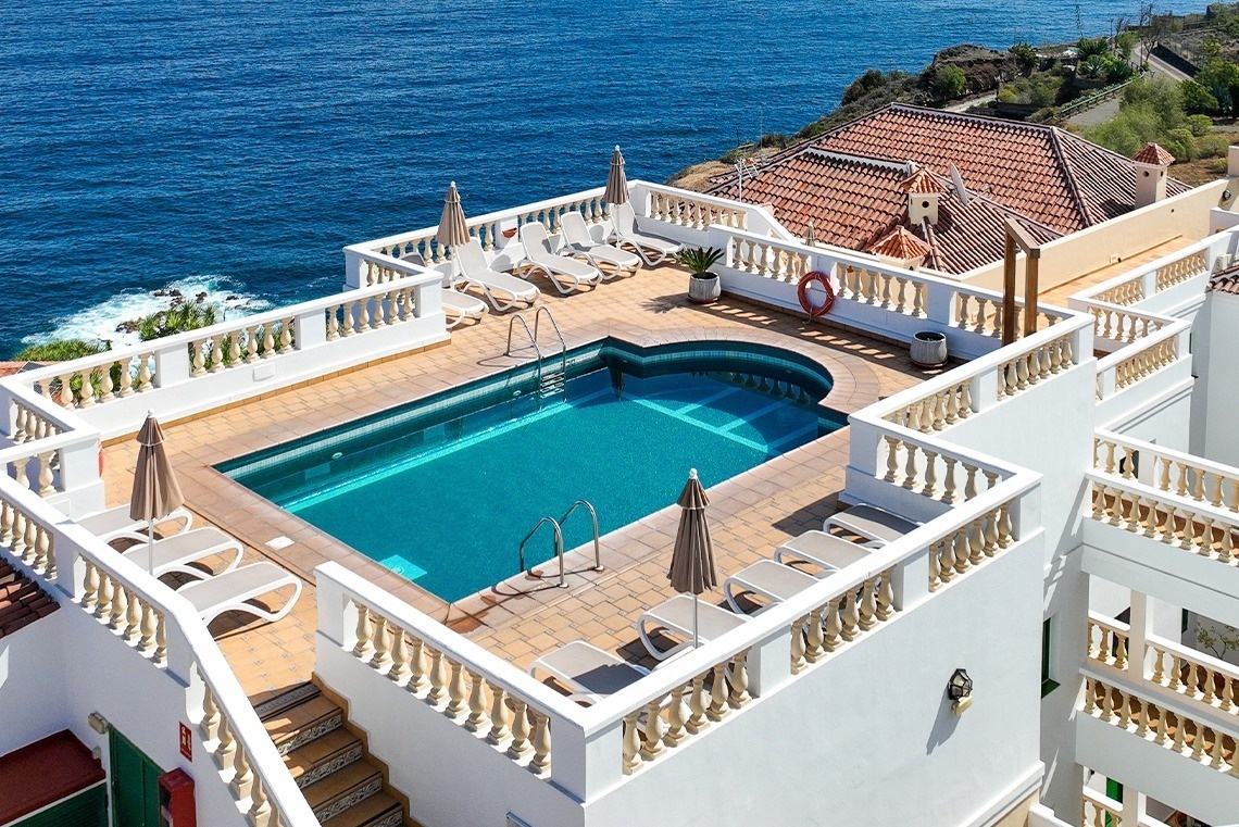 una piscina rodeada de sillas y sombrillas con vistas al océano