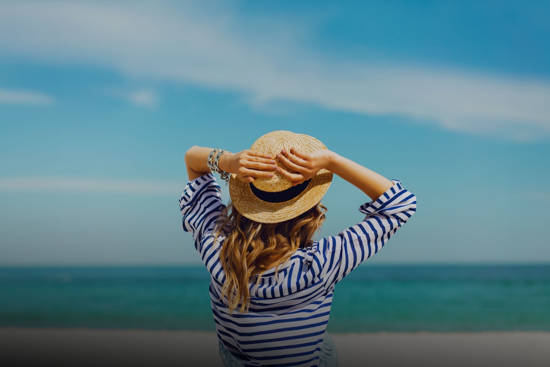 a woman wearing a striped shirt and a straw hat looks at the ocean