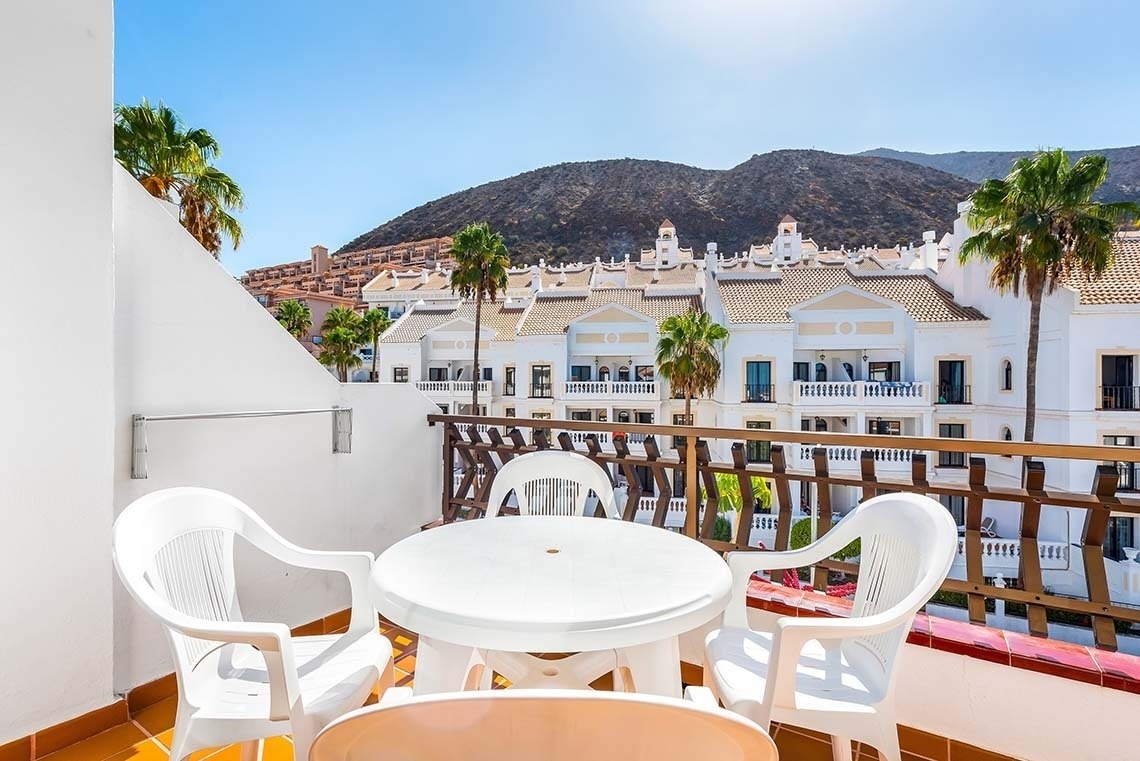 a balcony with a table and chairs and mountains in the background