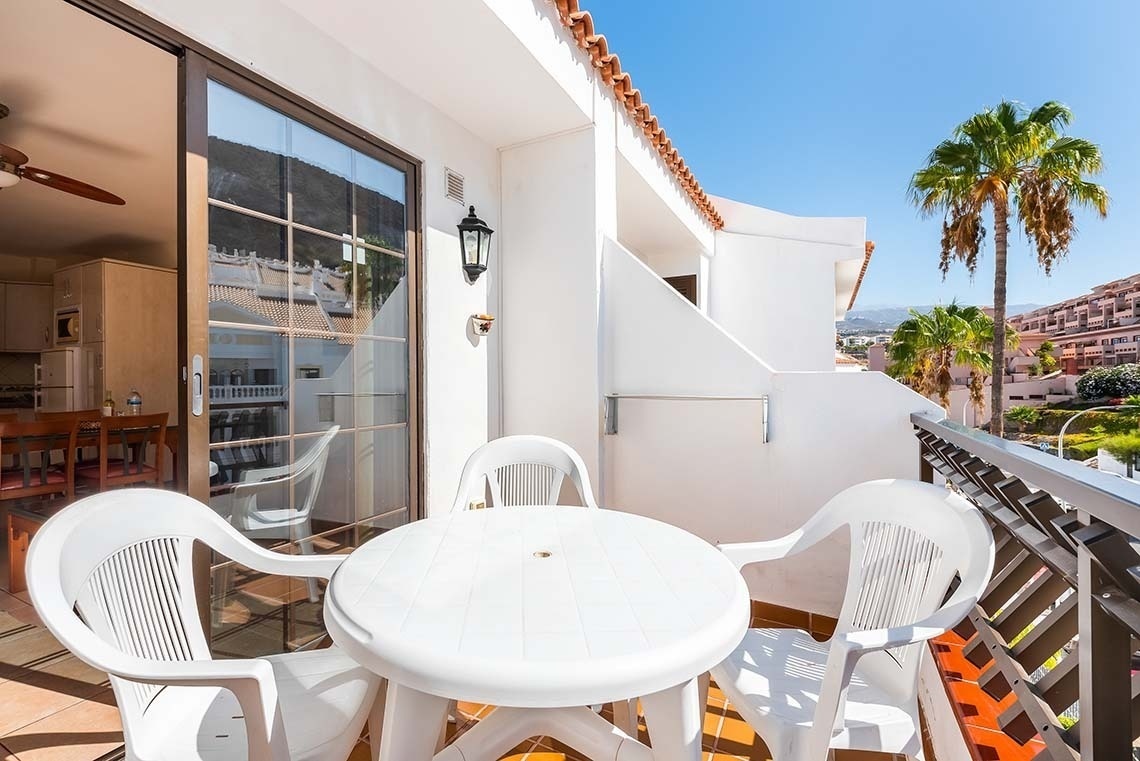 a white table and chairs on a balcony with palm trees in the background